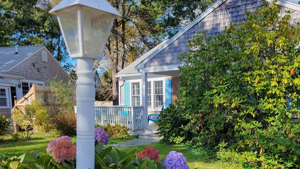 A residential house with a blue porch, a white fence, and a garden with hydrangea flowers.