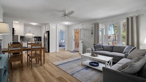 A modern living room with a grey sofa, wooden dining table, and a ceiling fan.