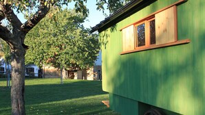 Un edificio verde con una ventana y una rueda de madera, rodeado de césped y árboles.