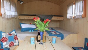 Interior de una cabaña de madera con literas, una mesa con velas y un jarrón con flores rojas.