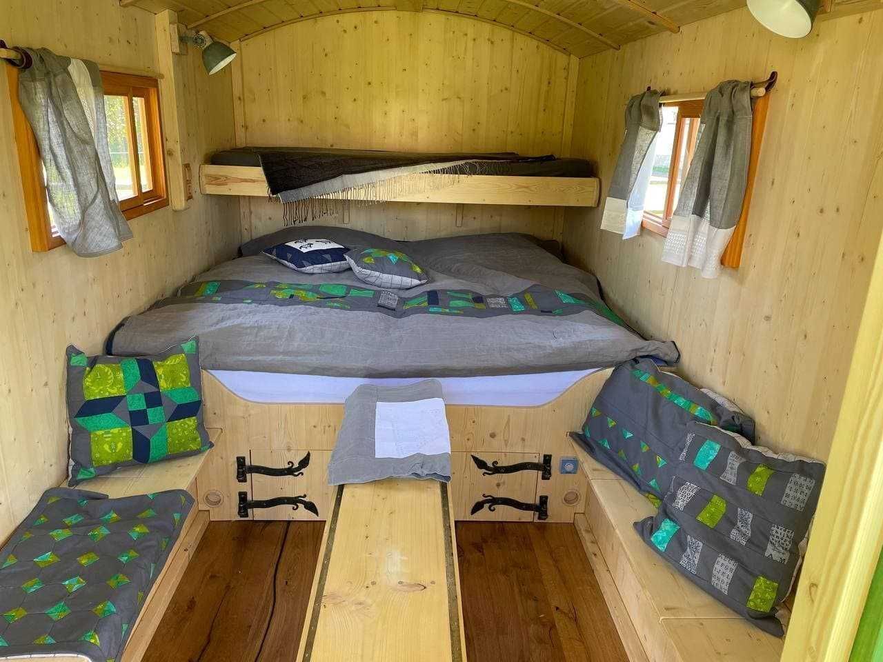 Une petite cabane en bois avec un lit superposé, deux petits coins salon et une fenêtre.