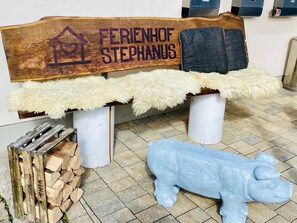 A bench with a wooden backrest labeled 'FERENHOF STEPHANUS,' a fluffy white cushion, and a blue bull sculpture on the ground. - Ferienwohnung Schusterstube - Ferienhof Stephanus (Ebermannstadt)