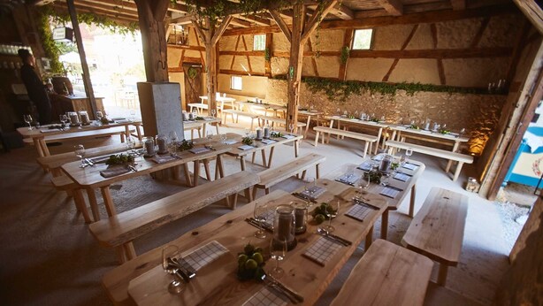 Un área de comedor al aire libre con mesas y bancos de madera, dispuesta en un espacio amplio.