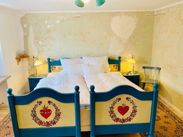 Una cama con dos mesitas de noche, una silla y una pared con pintura descascarada.