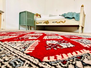 Un dormitorio con cama, radiador verde y alfombra estampada.