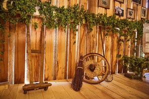 A rustic wooden wall with vertical planks, a broom, a wheeled cart, and greenery. - Ferienwohnung Schusterstube - Ferienhof Stephanus (Ebermannstadt)