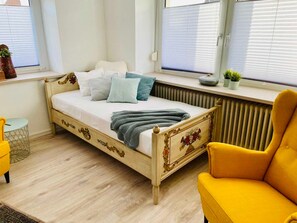 Una cama con cabecera, una ventana con persianas, un radiador y un sillón amarillo.