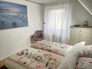 A bedroom with a bed, a chair, a dresser, a painting, and a window with curtains. - FeWo Hänsel, Germany (Zinnowitz)
