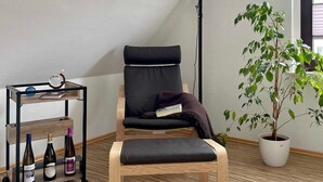 A modern room with a black leather chair, a wooden floor, a small table with bottles, a potted plant, and a large lamp. - FeWo Hänsel, Germany (Zinnowitz)