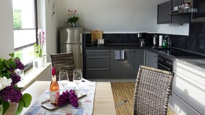 A modern kitchen with a dining area, featuring a refrigerator, stove, and dining table set with flowers and glasses. - FeWo Hänsel, Germany (Zinnowitz)