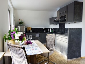 A modern kitchen with dark cabinetry, a dining area with a wicker chair, and a table set with flowers and glasses. - FeWo Hänsel, Germany (Zinnowitz)