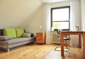 A room with a sofa, a desk, a radiator, and a window with curtains. - Hänsel Vacation Rental, Germany (Zinnowitz)