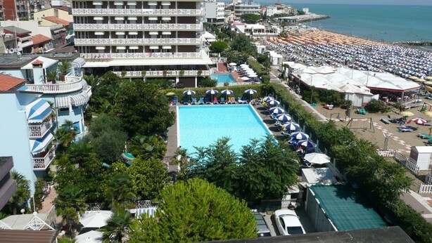 Un hotel con una piscina ampia, numerosi balconi e vista mare.