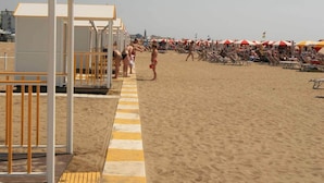 Una spiaggia con lettini e ombrelloni, una postazione di salvataggio e un cielo sereno.