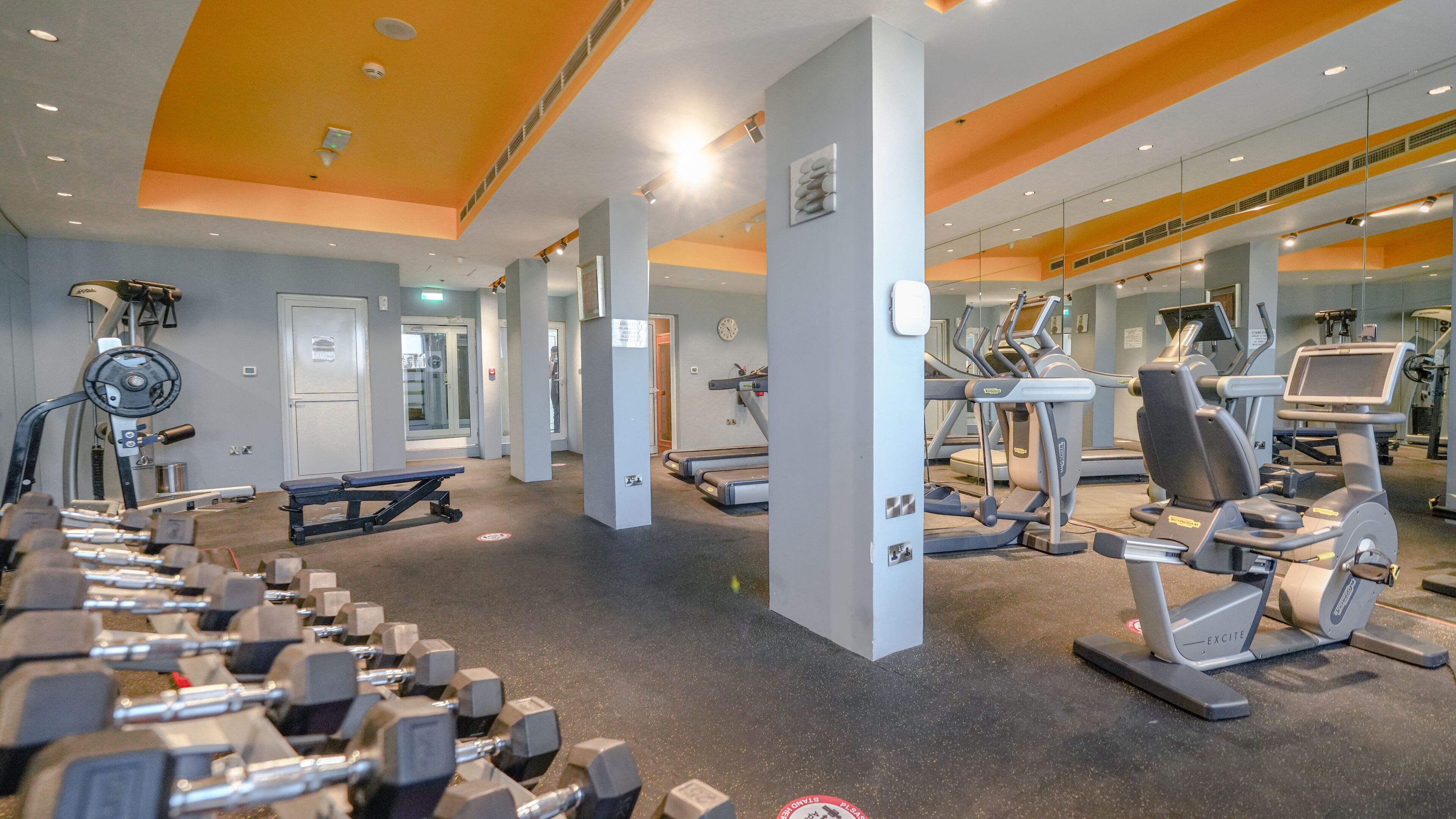 Een fitnessruimte met diverse fitnessapparaten, waaronder loopbanden en krachttrainingsmachines.