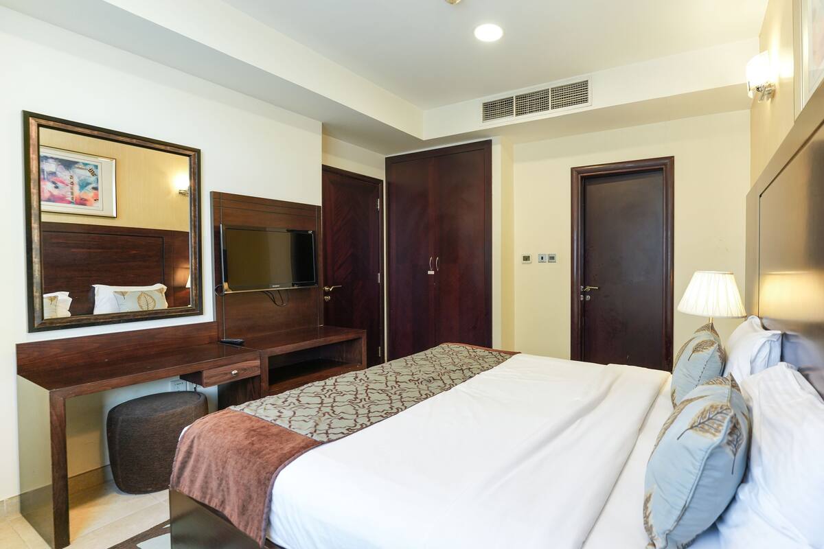 A hotel room with a bed, a desk, a mirror, a wardrobe, and a television.