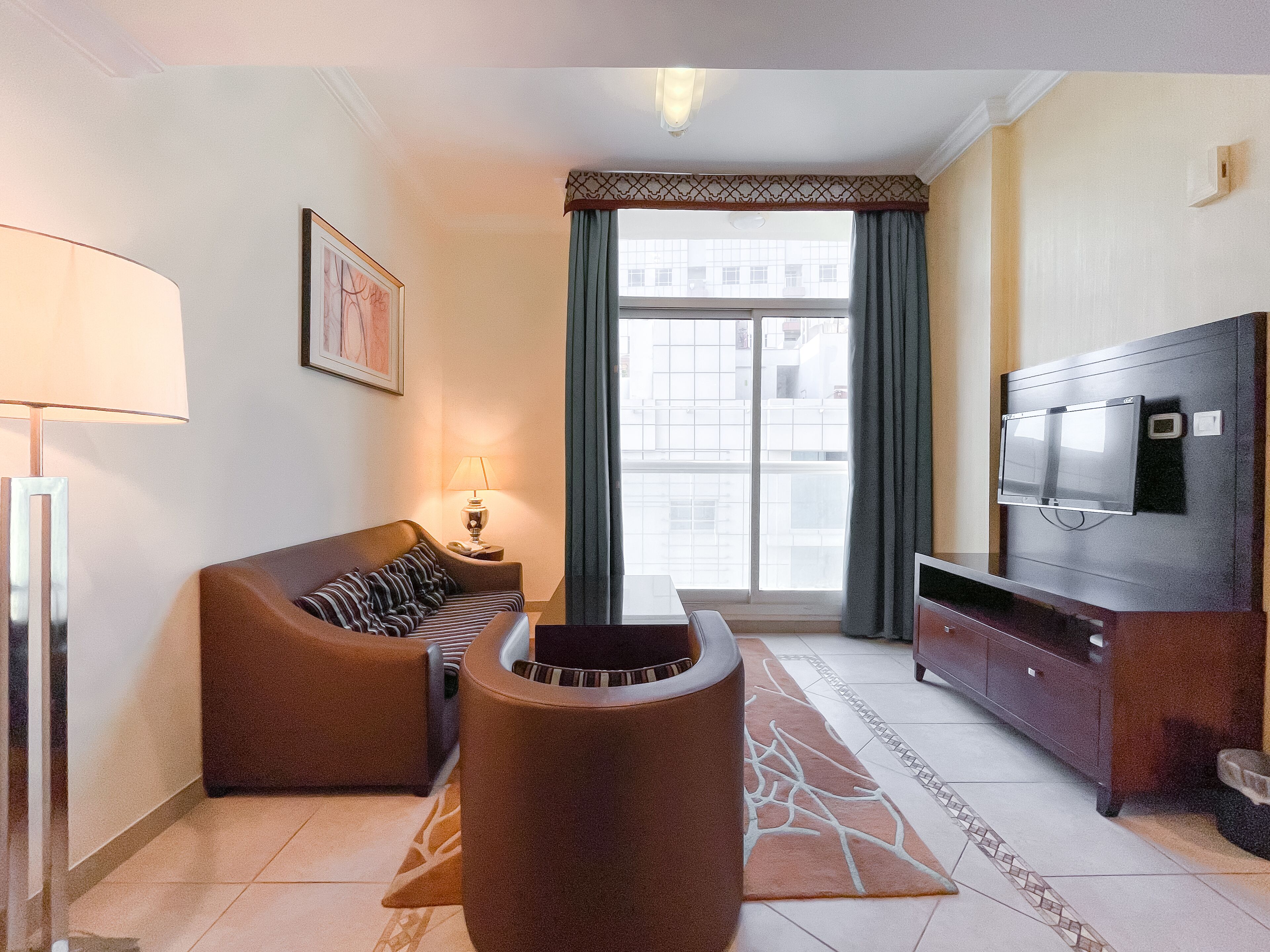 Een moderne woonkamer met een bank, een televisie, een lamp en uitzicht op buiten.