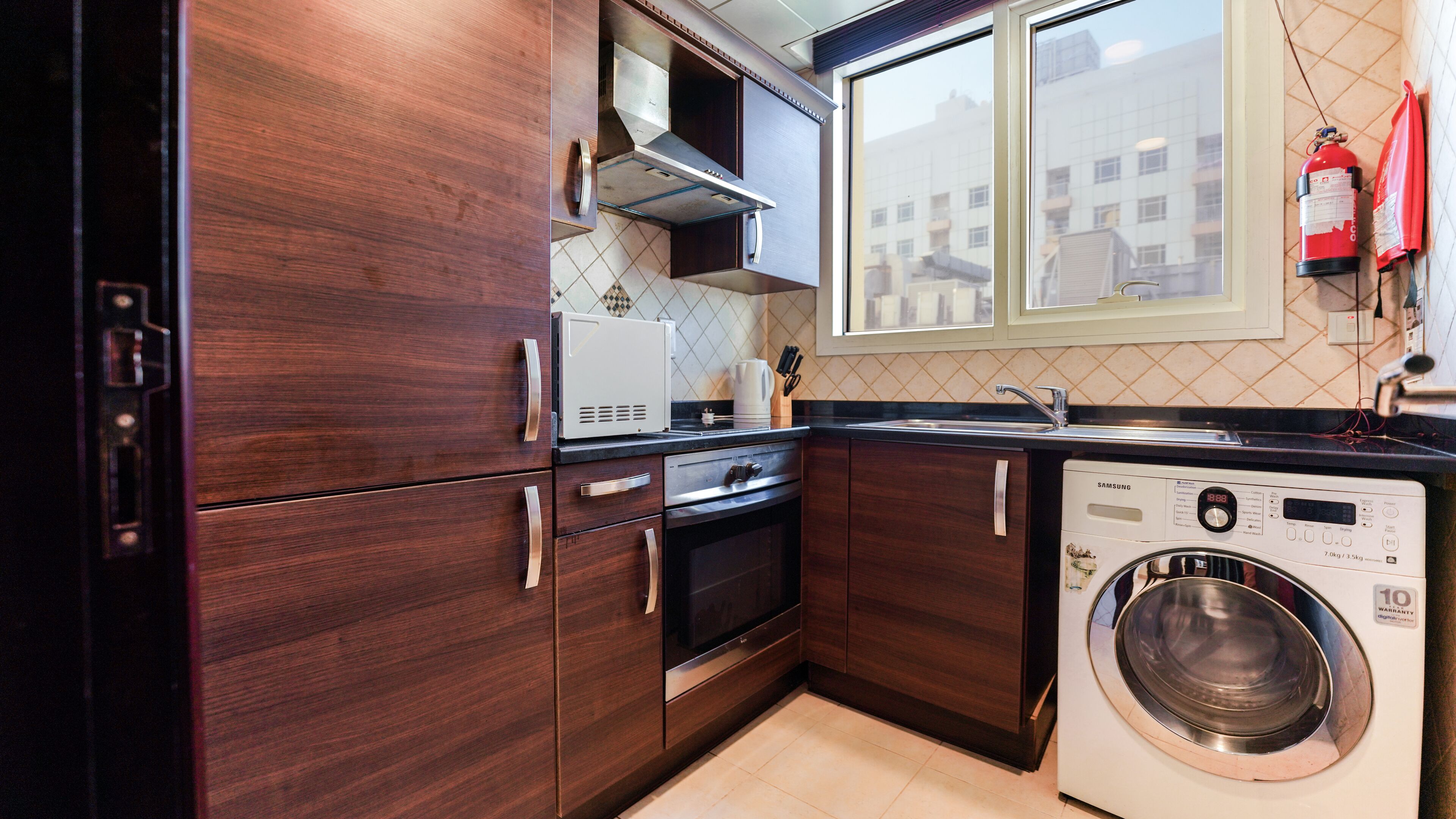 A compact kitchen with dark wood cabinets, a stainless steel range, a built-in oven, a microwave, and a front-loading washing machine.