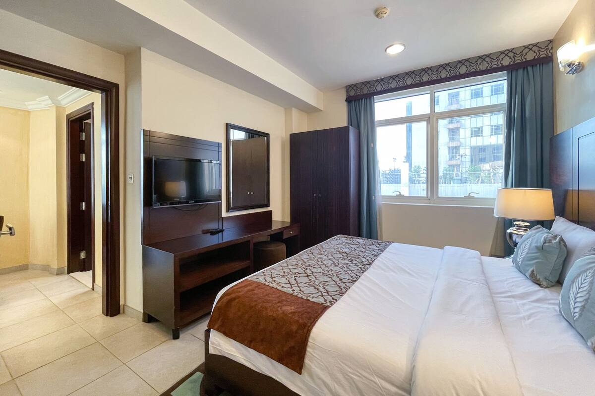 A hotel room with a bed, a TV, a desk, and a window with curtains.