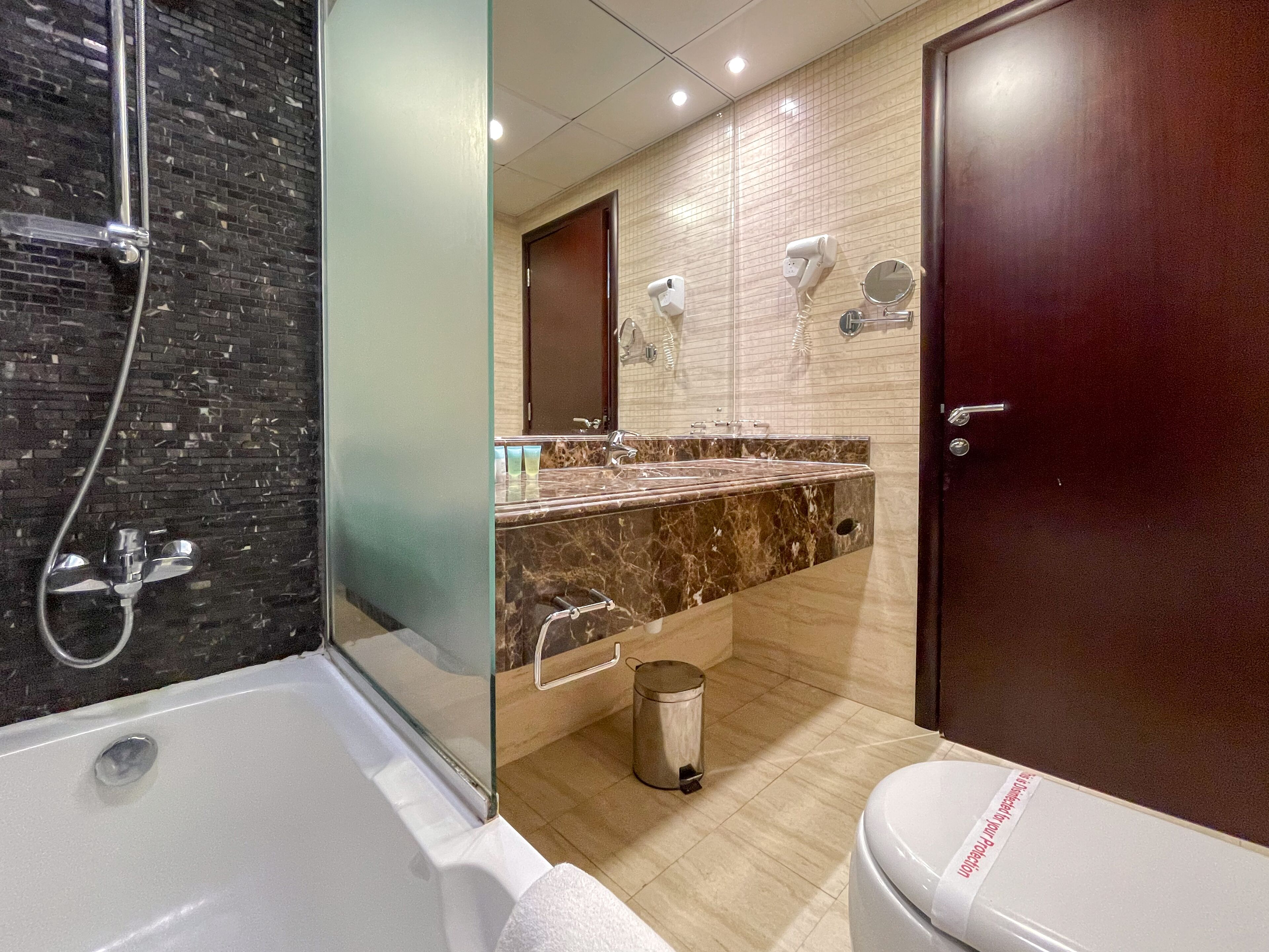 A modern bathroom with a glass-enclosed shower, a marble vanity, a toilet, and a trash can.