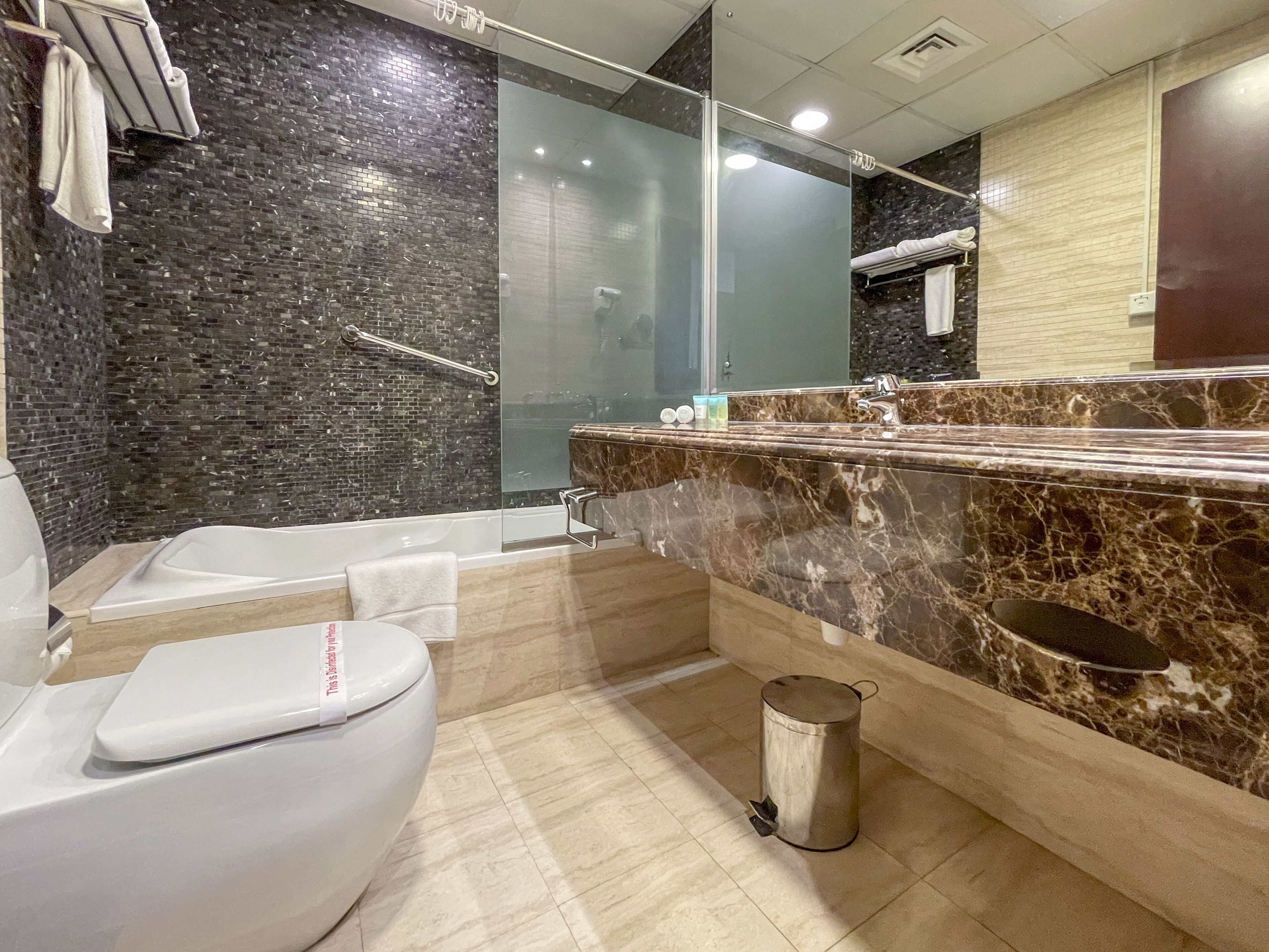 Une salle de bain moderne avec des toilettes blanches, une douche à parois de verre, un lavabo en marbre et une poubelle.