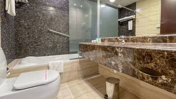 Une salle de bain moderne avec des toilettes blanches, une douche à parois de verre, un lavabo en marbre et une poubelle.