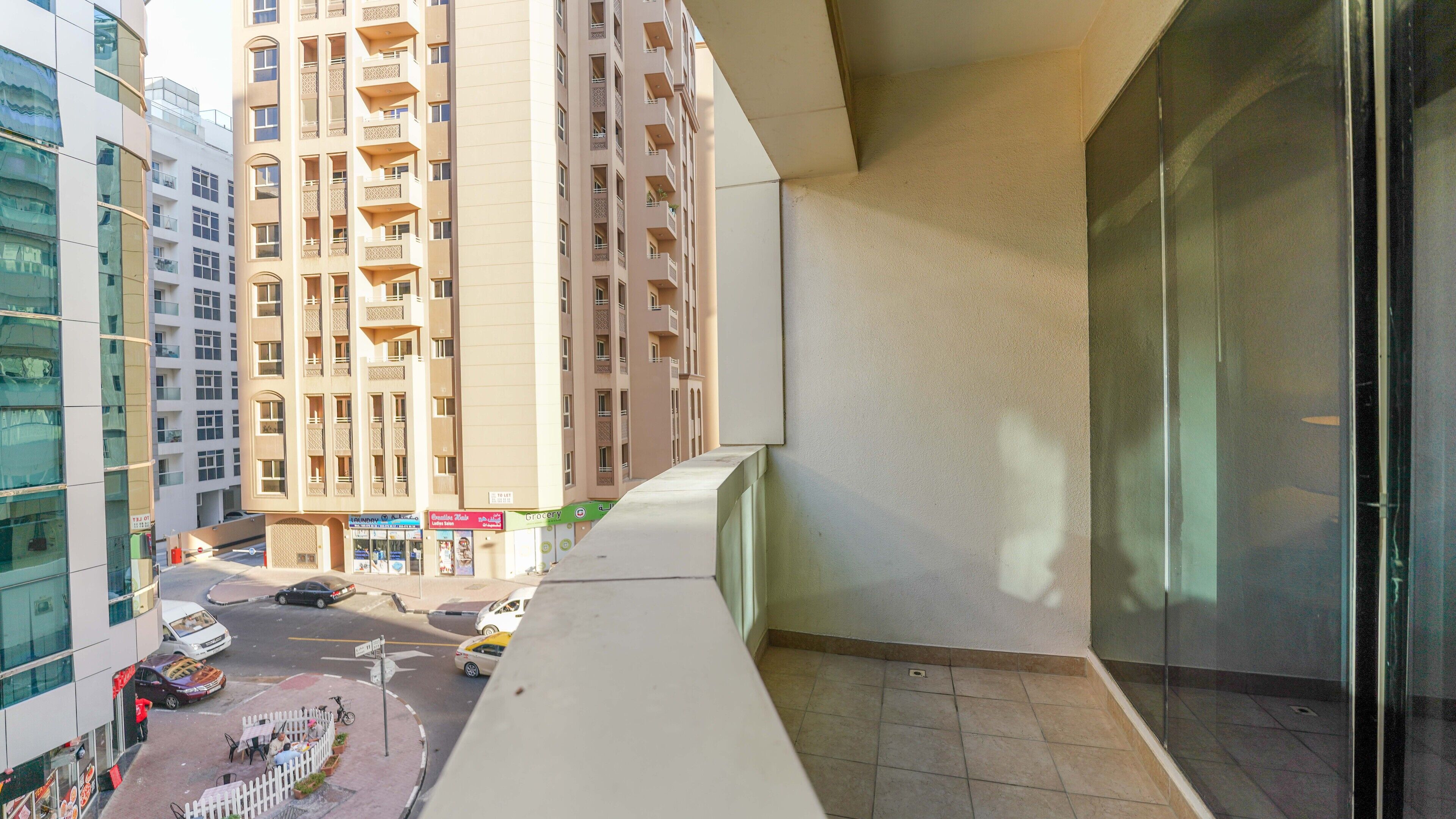 A balcony with a view of a city street, a tall building with multiple balconies, and a clear sky.