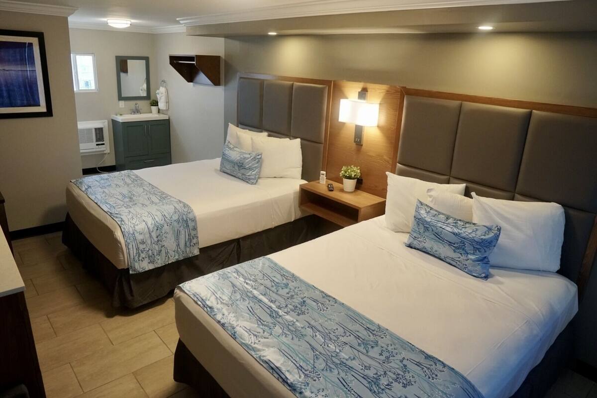 A hotel room with two beds, a small desk, a mirror, and a wall-mounted shelf.