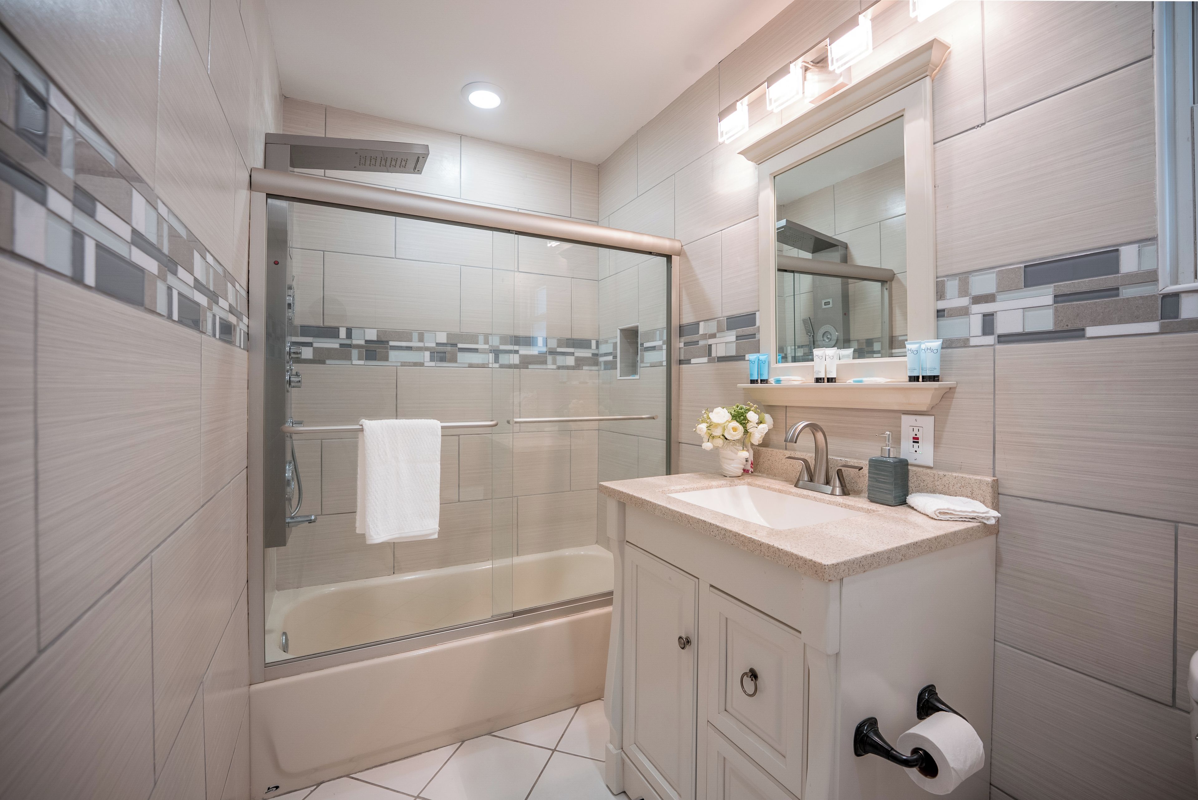 A modern bathroom with a glass-enclosed shower, a bathtub, a sink with a mirror, and a toilet.