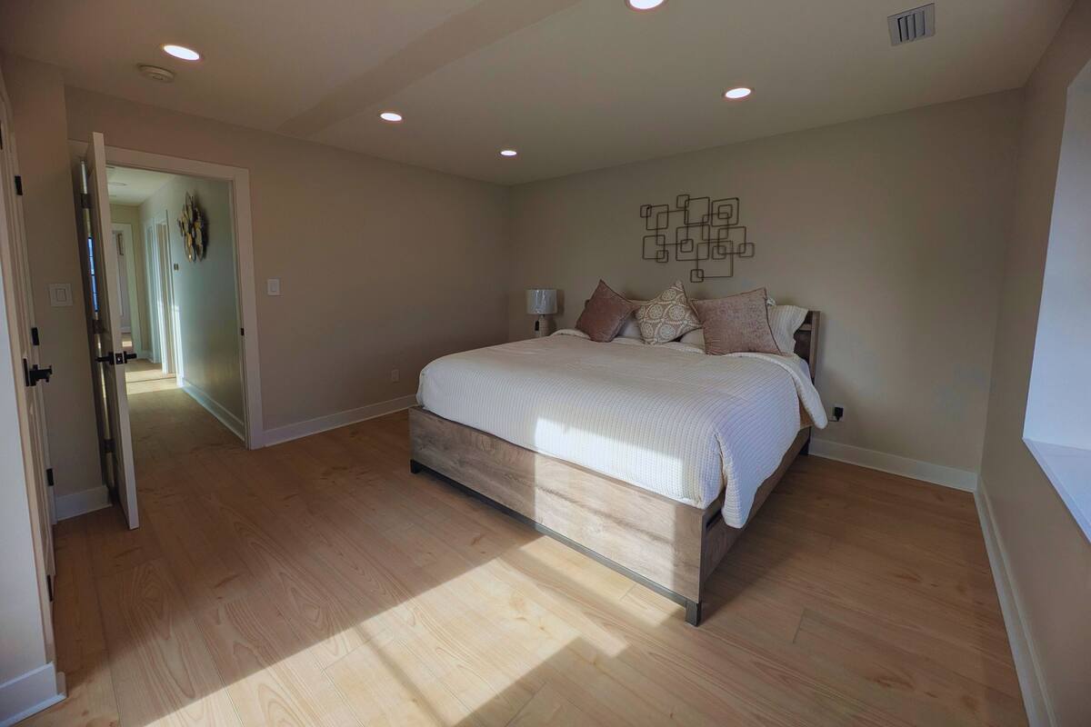 A bedroom with a wooden bed, recessed ceiling lights, and a hallway leading to another room.