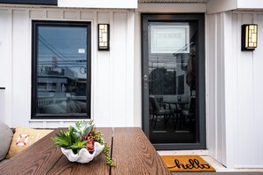 A wooden table with a plant centerpiece, a black door with a glass panel, and a 'hello' mat. - Coastal Sands Inn (Wildwood)