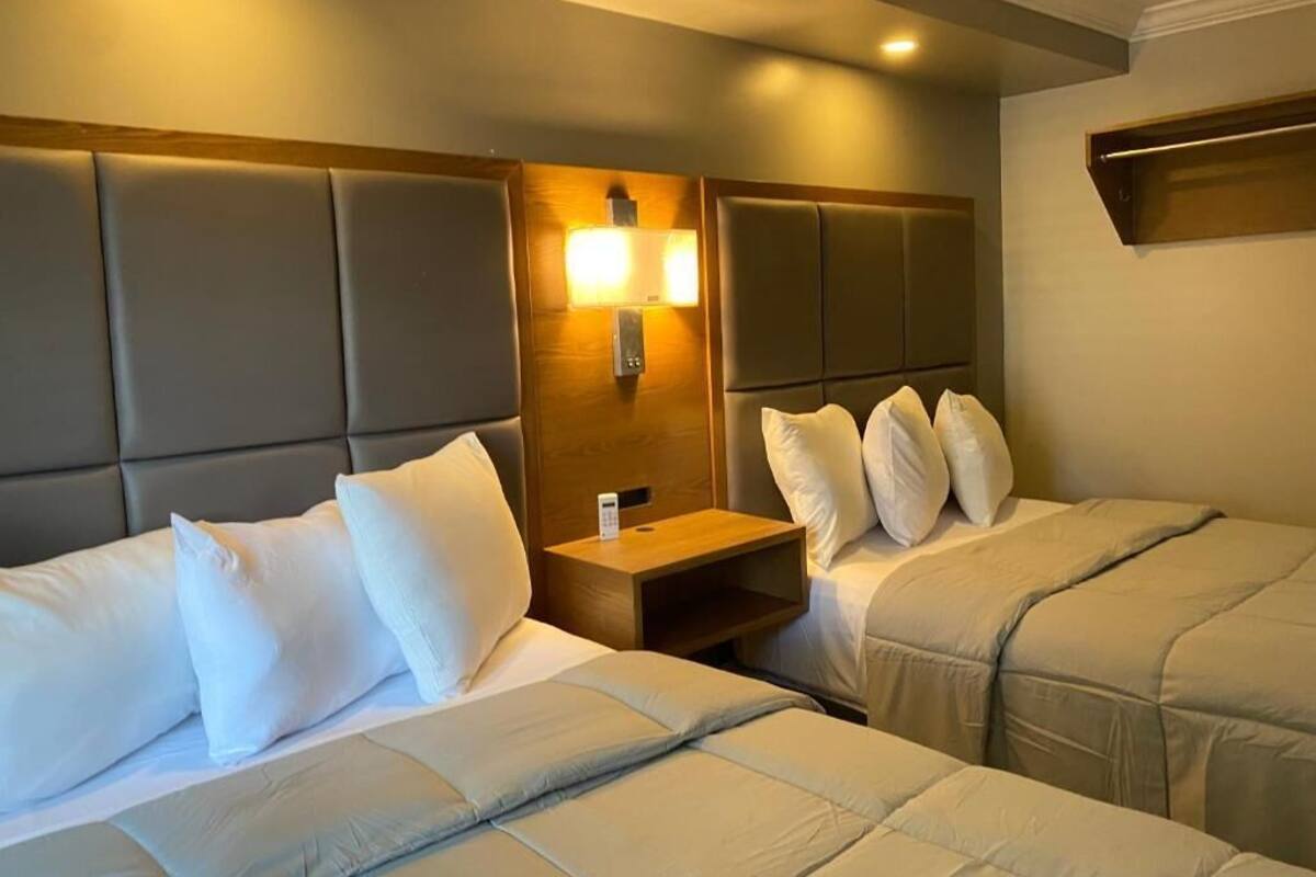 A hotel room with two beds, a nightstand, and a wall-mounted lamp.