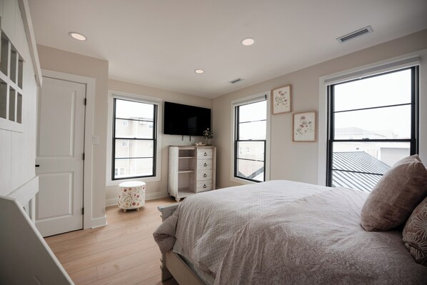 A bedroom with a bed, a TV, a window, and a small cabinet.