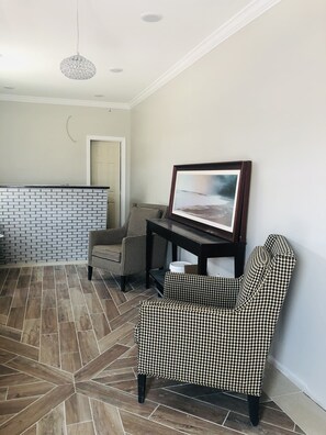 A living room with a houndstooth patterned sofa, a framed picture on the wall, and a brick-patterned wall. - Coastal Sands Inn (Wildwood)