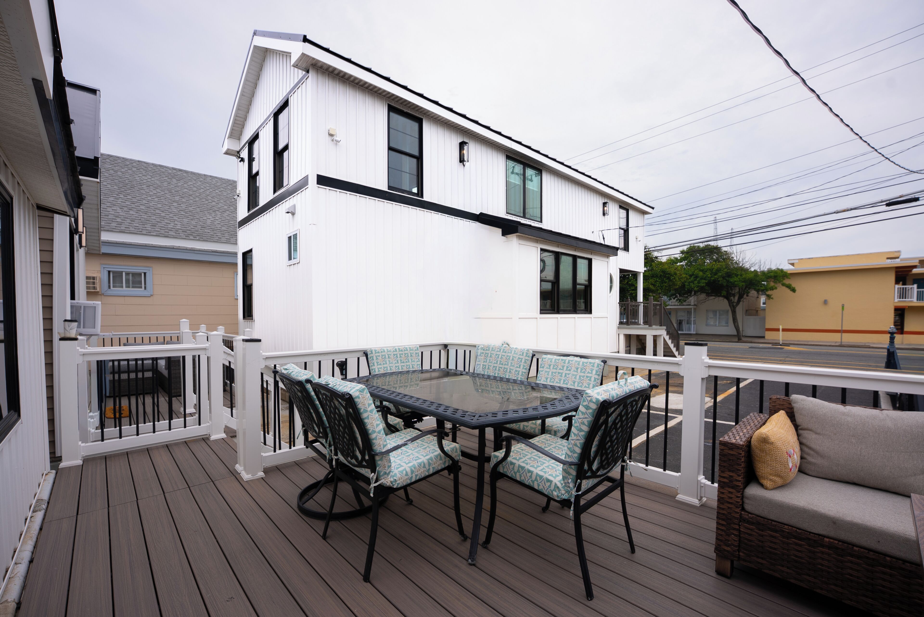 Una terraza con una mesa y sillas de vidrio, un sofá de mimbre y una barandilla blanca.