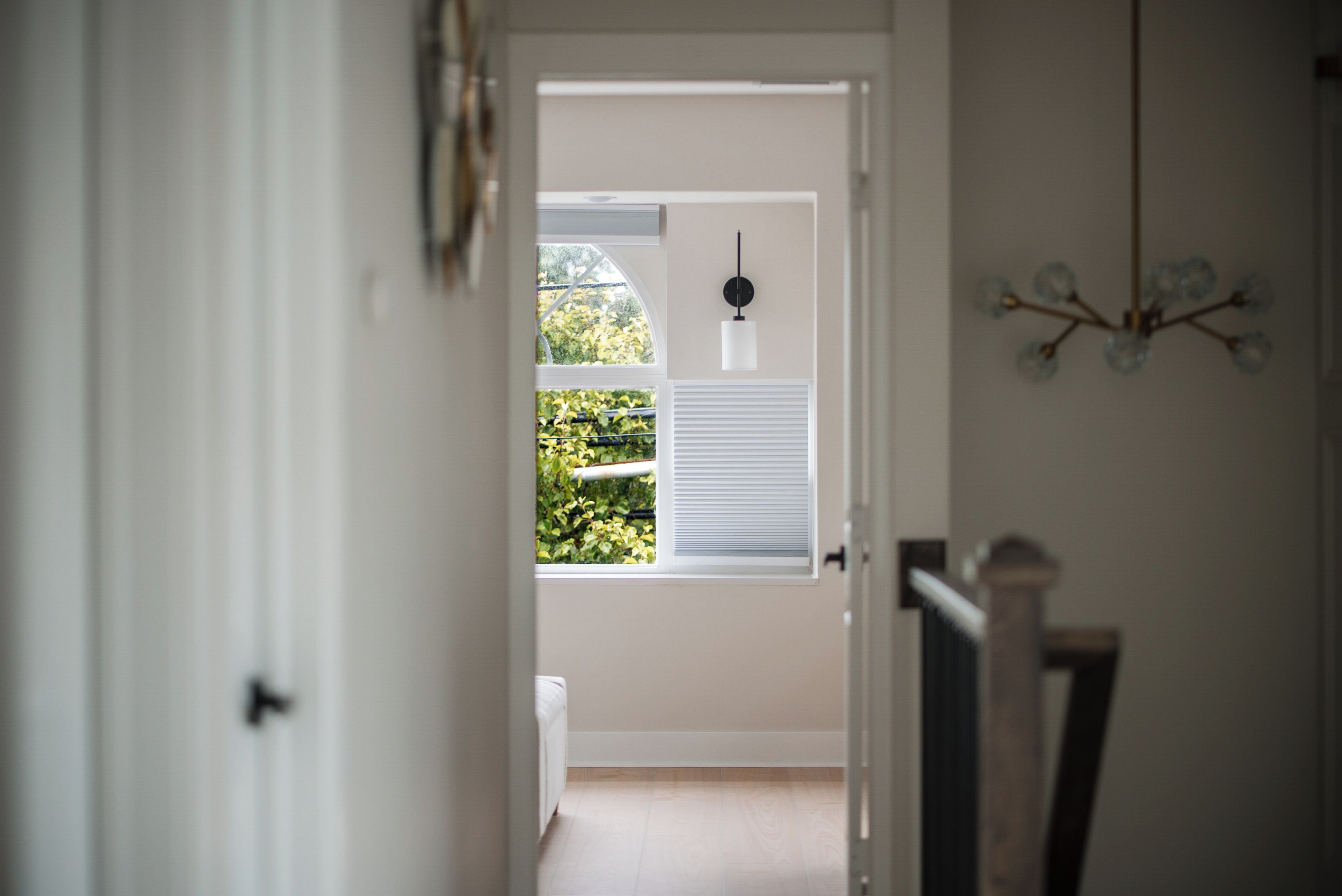 Un pasillo que lleva a una habitación con ventana, puerta y una lámpara fijada a la pared.