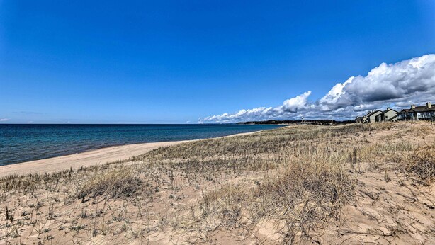 A beach with a clear sky, a sandy shore, and a row of houses in the background.