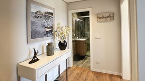 A hallway with a white console table, a vase with flowers, a framed black and white painting, and a wooden cabinet leading to a bathroom. - Paradise Apartment by LovelyStay (Funchal)