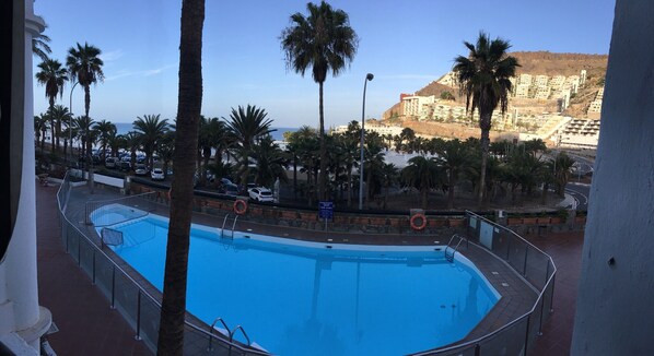 A swimming pool with a view of a beach and buildings in the background.