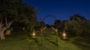 Un jardin illuminé la nuit, avec un sentier, des arbres et des sièges d’extérieur.