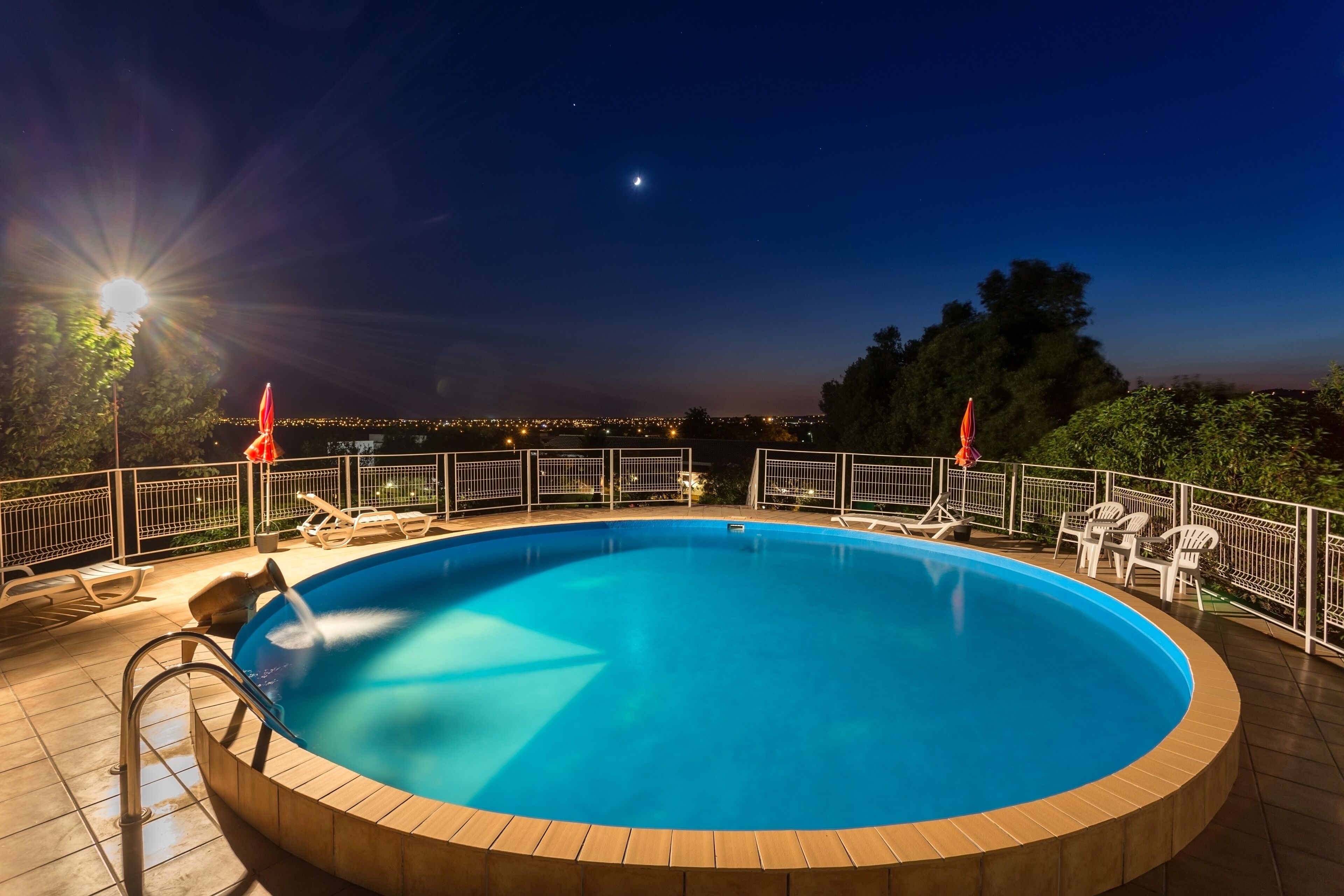 A circular pool with a wooden edge, surrounded by a white fence and white chairs.