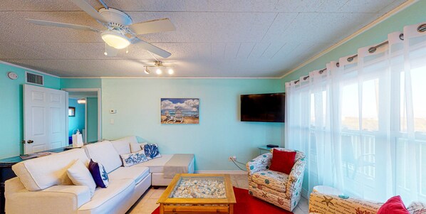 A living room with a ceiling fan, a flat-screen TV, a sofa, a chair, and a coffee table.