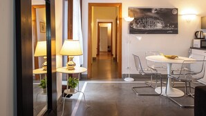 A modern hotel room with a dining area, a mirror, a lamp, a framed picture, and a view of the hallway. - Domitia Home A Pochi Passi DA Piazza DI Spagna (Roma)