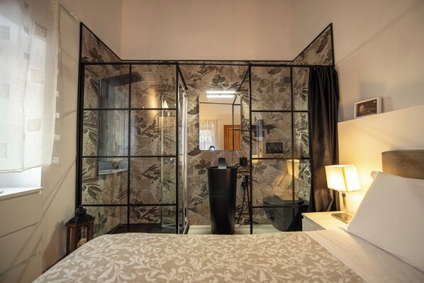 A hotel room with a bed, a nightstand, a lamp, a mirror, and a partition with a floral pattern.