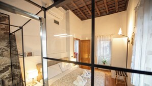 A hotel room with a bed, bedside table, lamp, and a view of the outside. - Domitia Home A Pochi Passi DA Piazza DI Spagna (Roma)