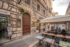 A street view with a café and outdoor seating, a shop with a large wooden door, and a building with a sign 'VENIR'.