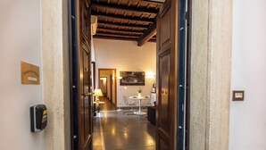 A hotel corridor with a wooden ceiling, a reception desk, a dining area with a table and chairs, and a wall-mounted light fixture. - Domitia Home A Pochi Passi DA Piazza DI Spagna (Roma)