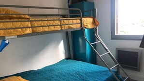 Une chambre avec un lit superposé, une échelle, une couvre-lit bleue et un oreiller jaune.