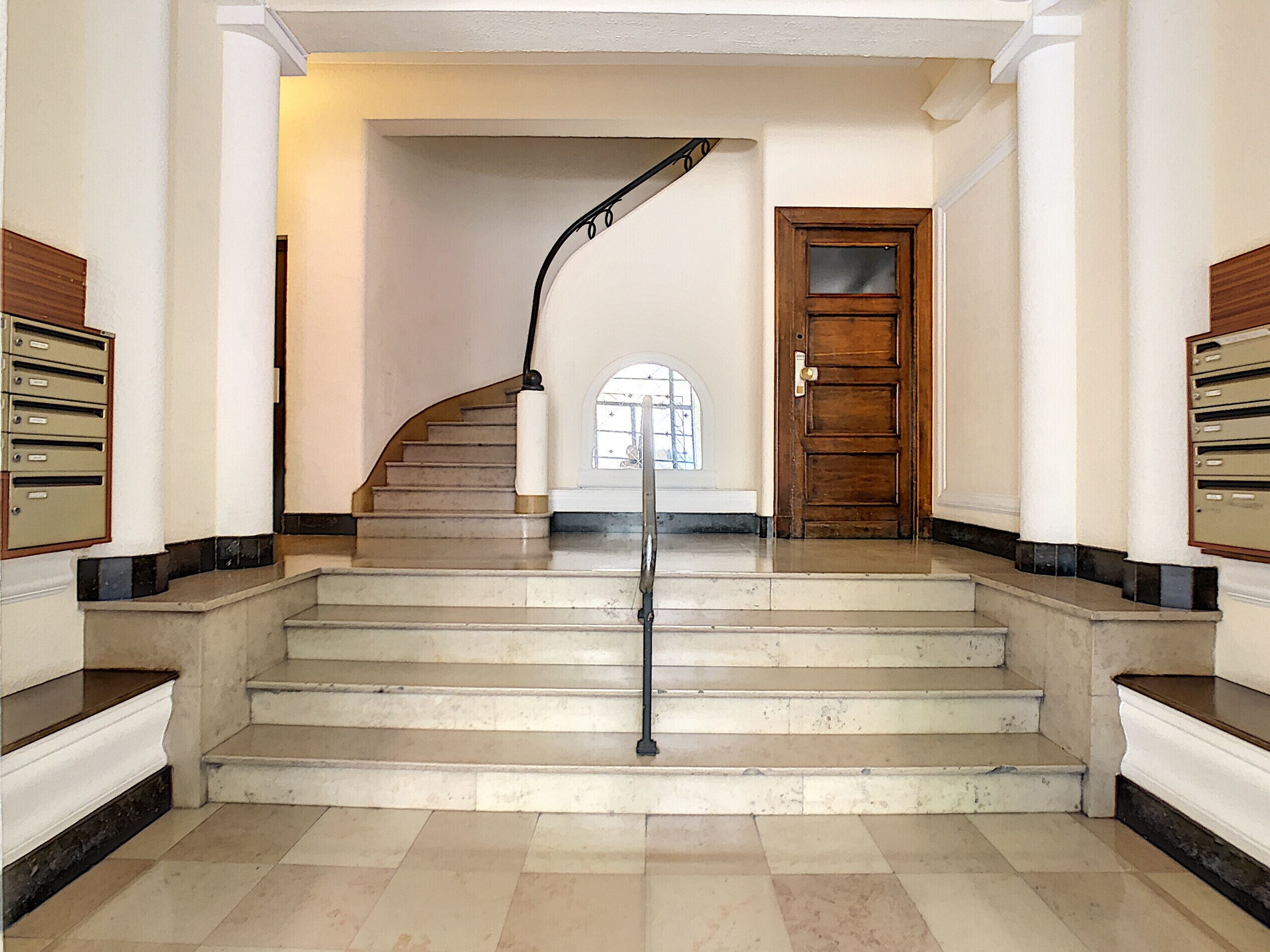 Eine imposante Treppe mit Handlauf, die zu einer Holztür mit Glasfenster führt.