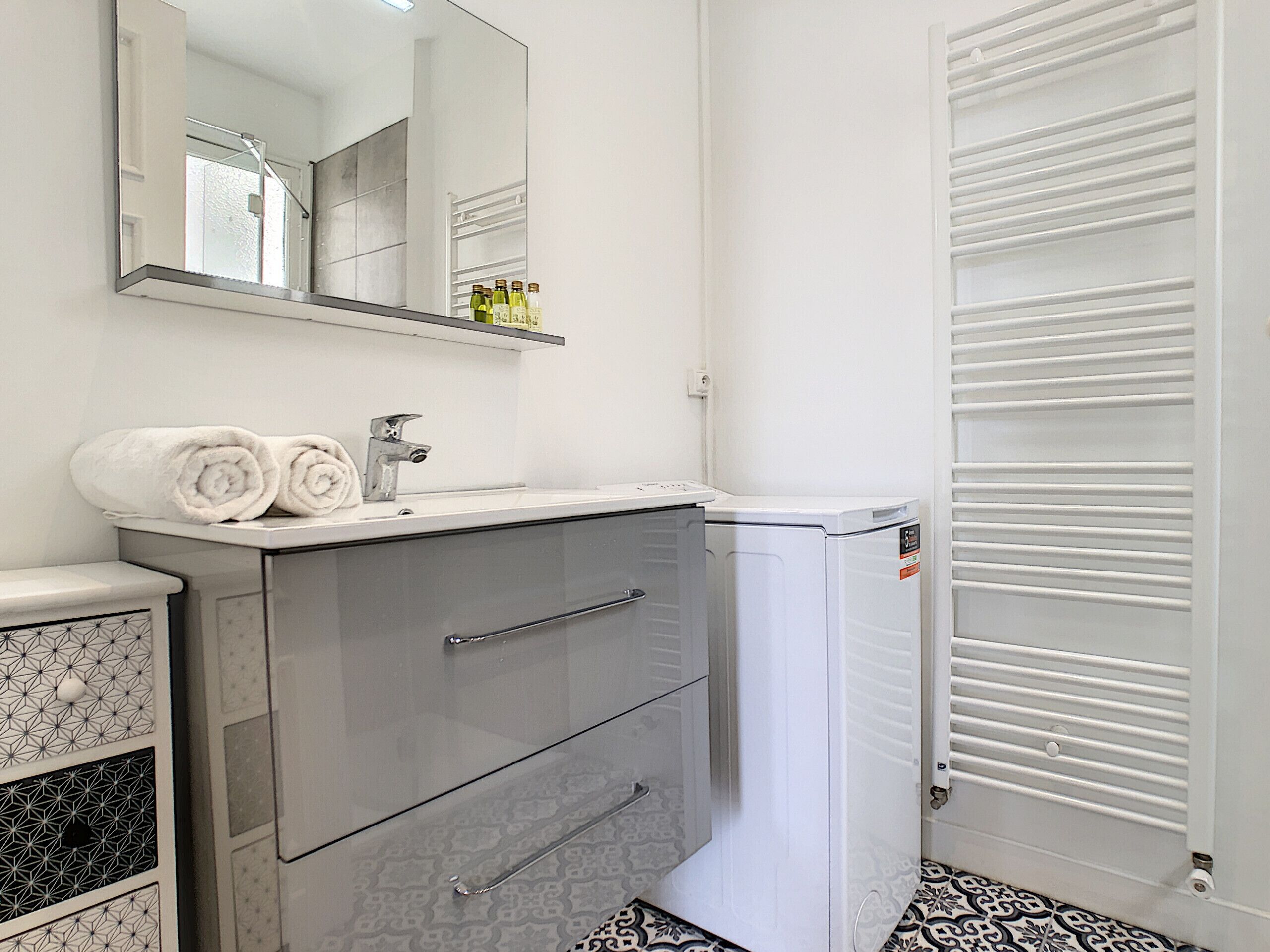 Une salle de bain avec un lavabo blanc, deux tiroirs, un miroir et un radiateur blanc.